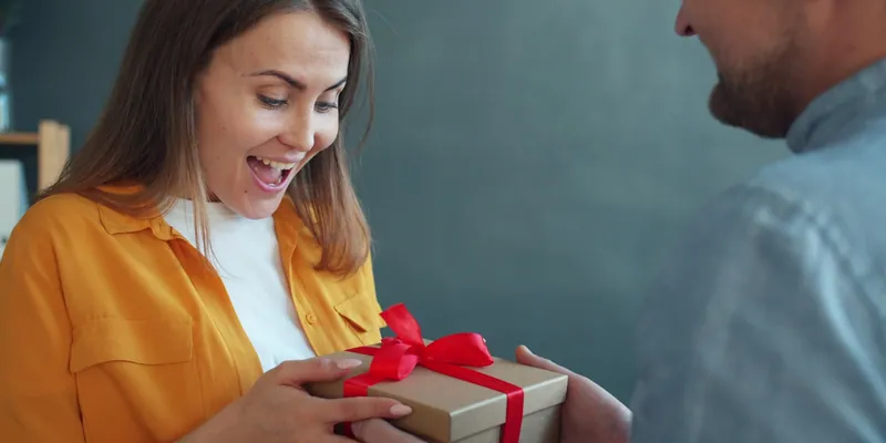 Frau freut sich sichtlich über ein Geschenk mit roter Schleife